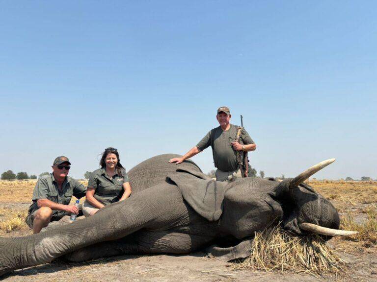 Three people posing next to an elephant that has just been shot.