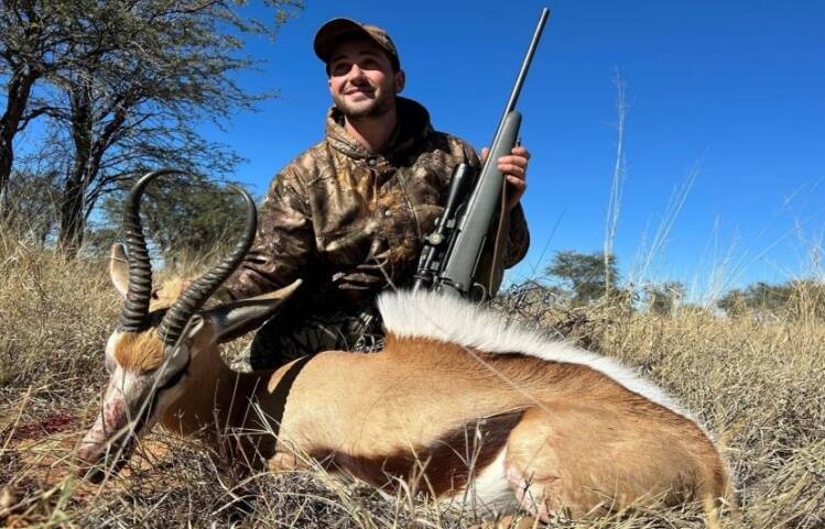 Man with rifle posing with springbuck he shot.