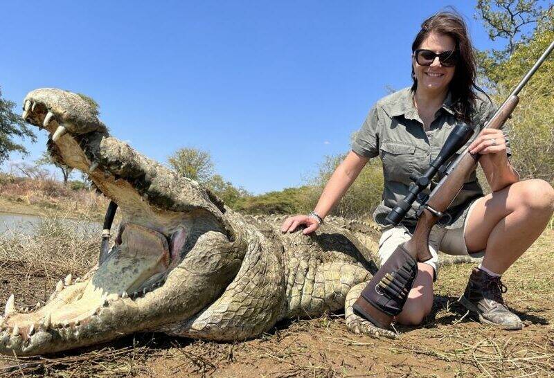 Lady posing with her gun and the crocodile she shot.